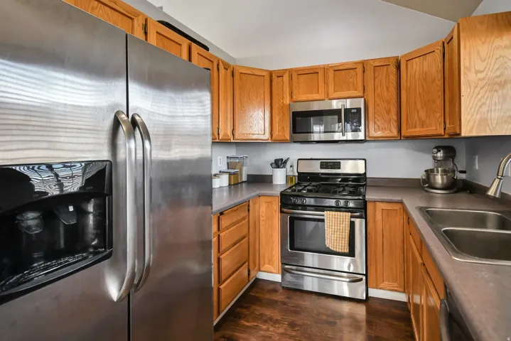Kitchen with appliances with stainless steel finishes, brown cabinetry, dark wood finished floors, and dark countertops
