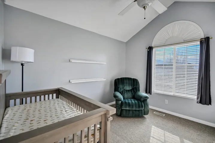 Bedroom featuring light carpet, a crib, lofted ceiling, and ceiling fan
