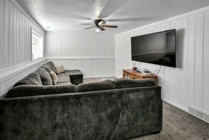 Carpeted living room with a textured ceiling, a ceiling fan, and wood walls