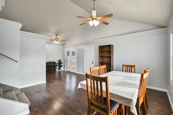 Dining space with dark wood-style flooring, ceiling fan, stairway, and high vaulted ceiling