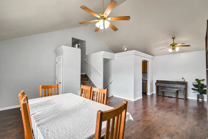 Dining space with a ceiling fan, dark wood-style floors, stairs, and lofted ceiling
