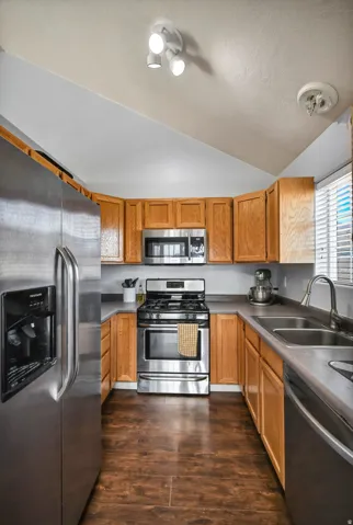 Kitchen featuring appliances with stainless steel finishes, lofted ceiling, dark wood finished floors, and brown cabinets