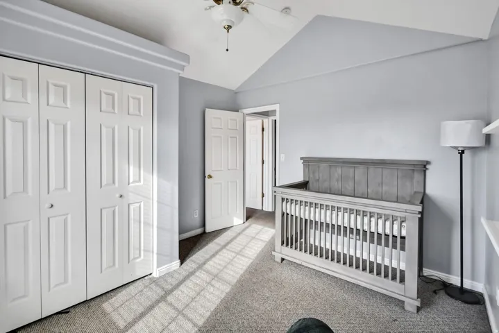 Bedroom with light colored carpet, lofted ceiling, a closet, a ceiling fan, and a crib