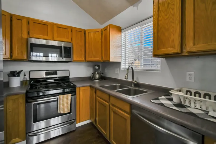 Kitchen with stainless steel appliances, dark countertops, lofted ceiling, and brown cabinets