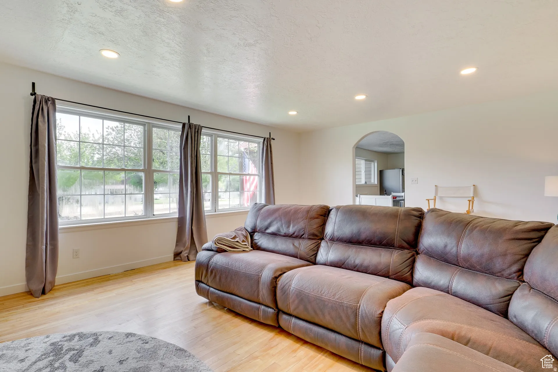 Living room with light wood-type flooring, arched walkways, a textured ceiling, and recessed lighting
