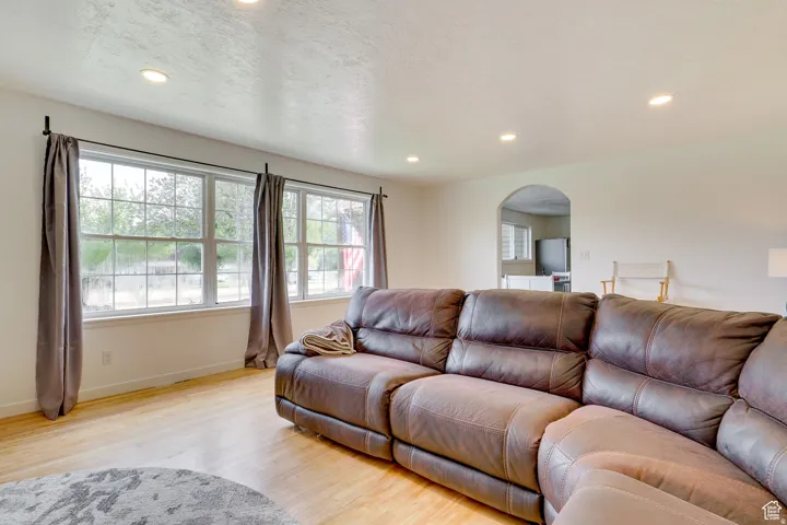 Living room with light wood-type flooring, arched walkways, a textured ceiling, and recessed lighting