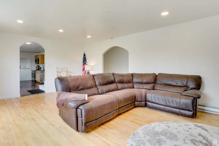 Living area with arched walkways, recessed lighting, light wood-style floors, a baseboard radiator, and a textured ceiling