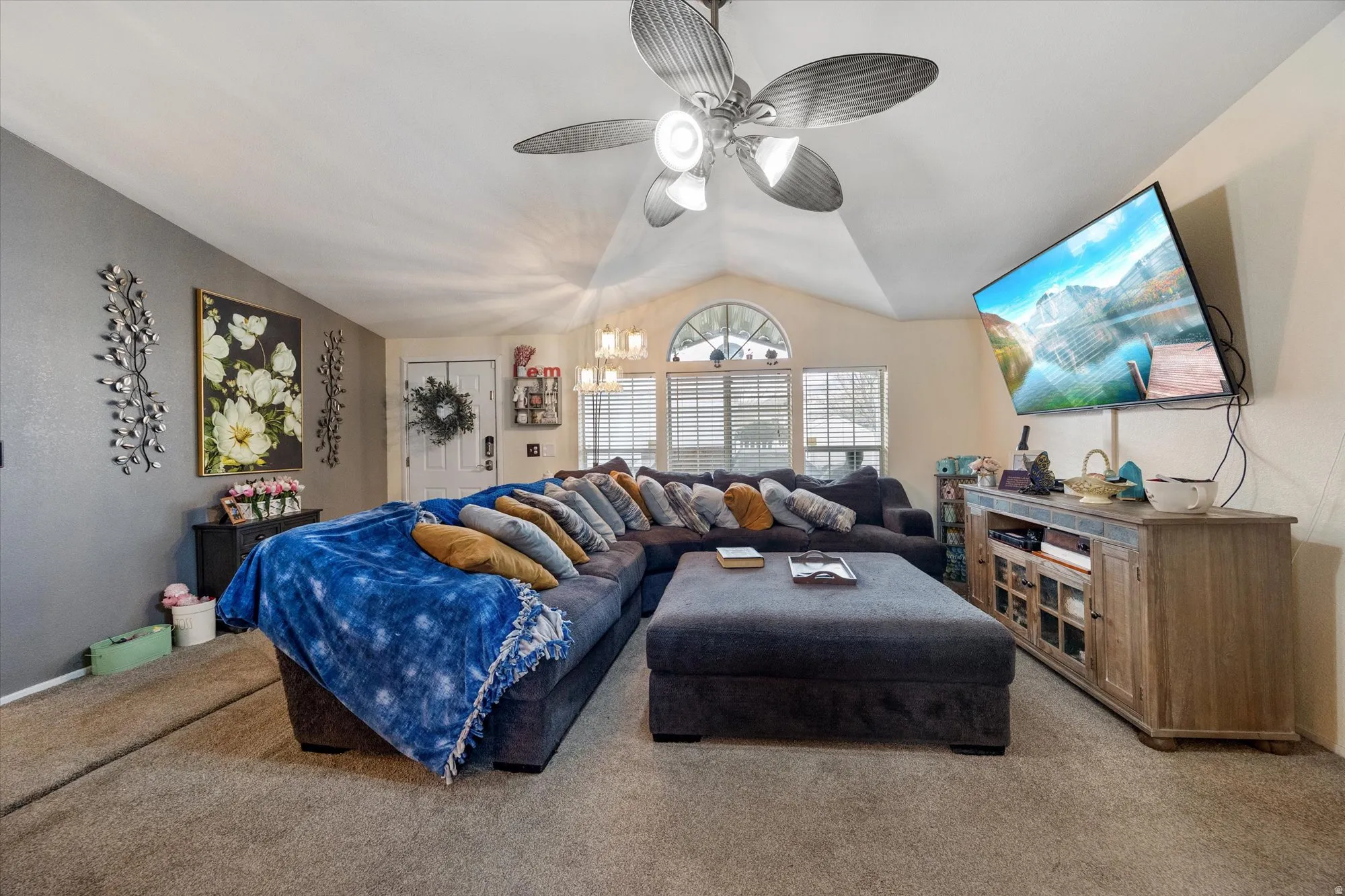 Carpeted living area featuring vaulted ceiling, a ceiling fan, and a chandelier