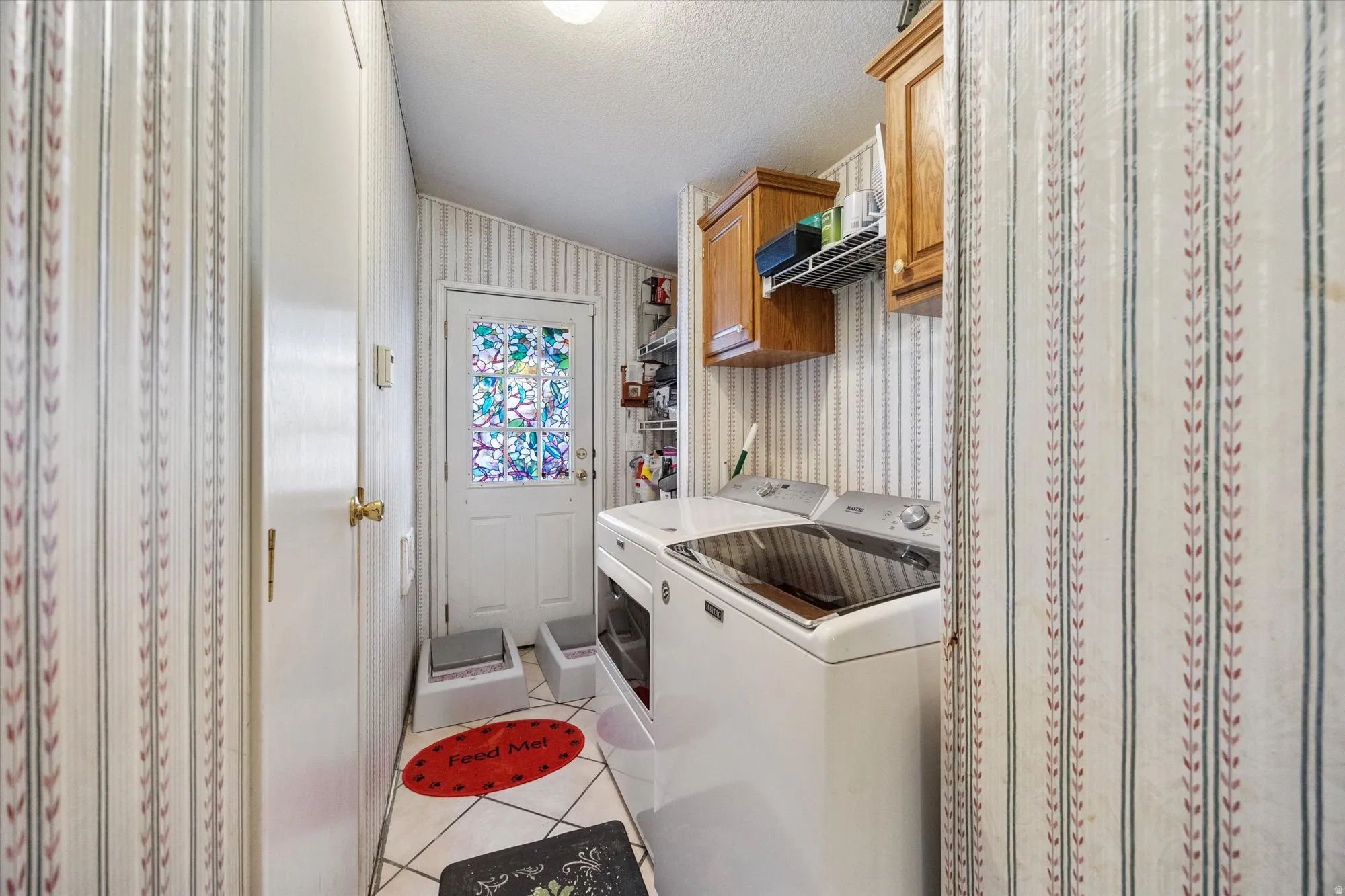 Washroom with wallpapered walls, light tile patterned floors, cabinet space, a textured ceiling, and separate washer and dryer