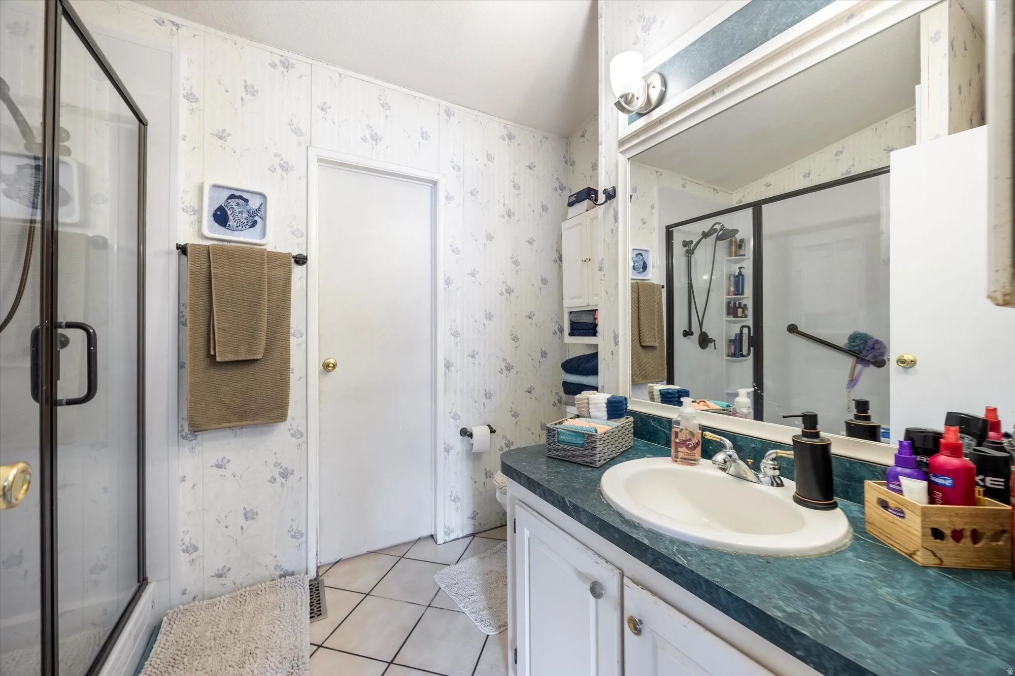 Bathroom featuring wallpapered walls, vanity, light tile patterned floors, and a stall shower