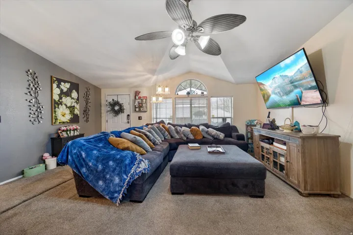 Carpeted living area featuring vaulted ceiling, a ceiling fan, and a chandelier