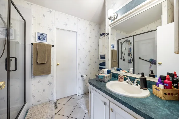 Bathroom featuring wallpapered walls, vanity, light tile patterned floors, and a stall shower
