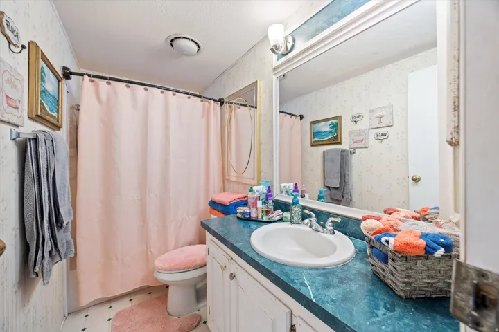 Bathroom featuring wallpapered walls, a shower with shower curtain, a textured ceiling, vanity, and light flooring