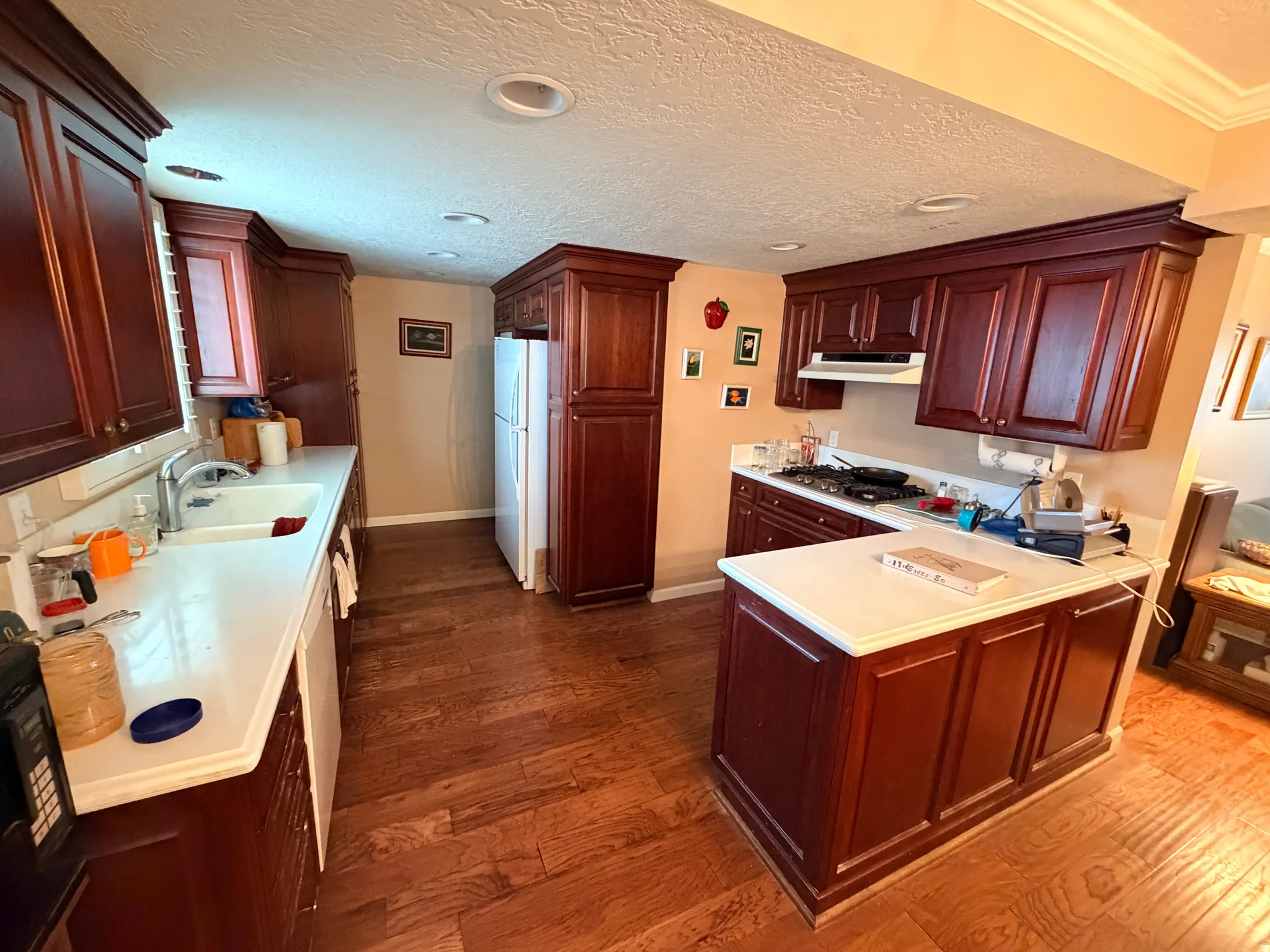 Kitchen with a peninsula, light countertops, dark wood-type flooring, white appliances, and a textured ceiling