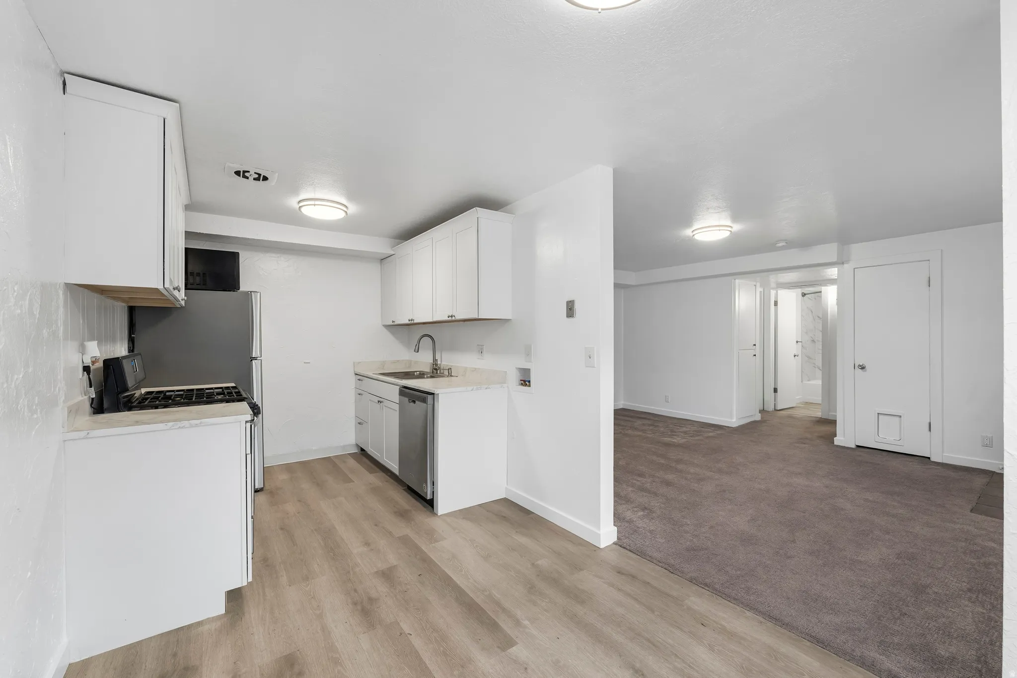 Kitchen featuring white cabinetry, light countertops, light carpet, appliances with stainless steel finishes, and light wood-style floors