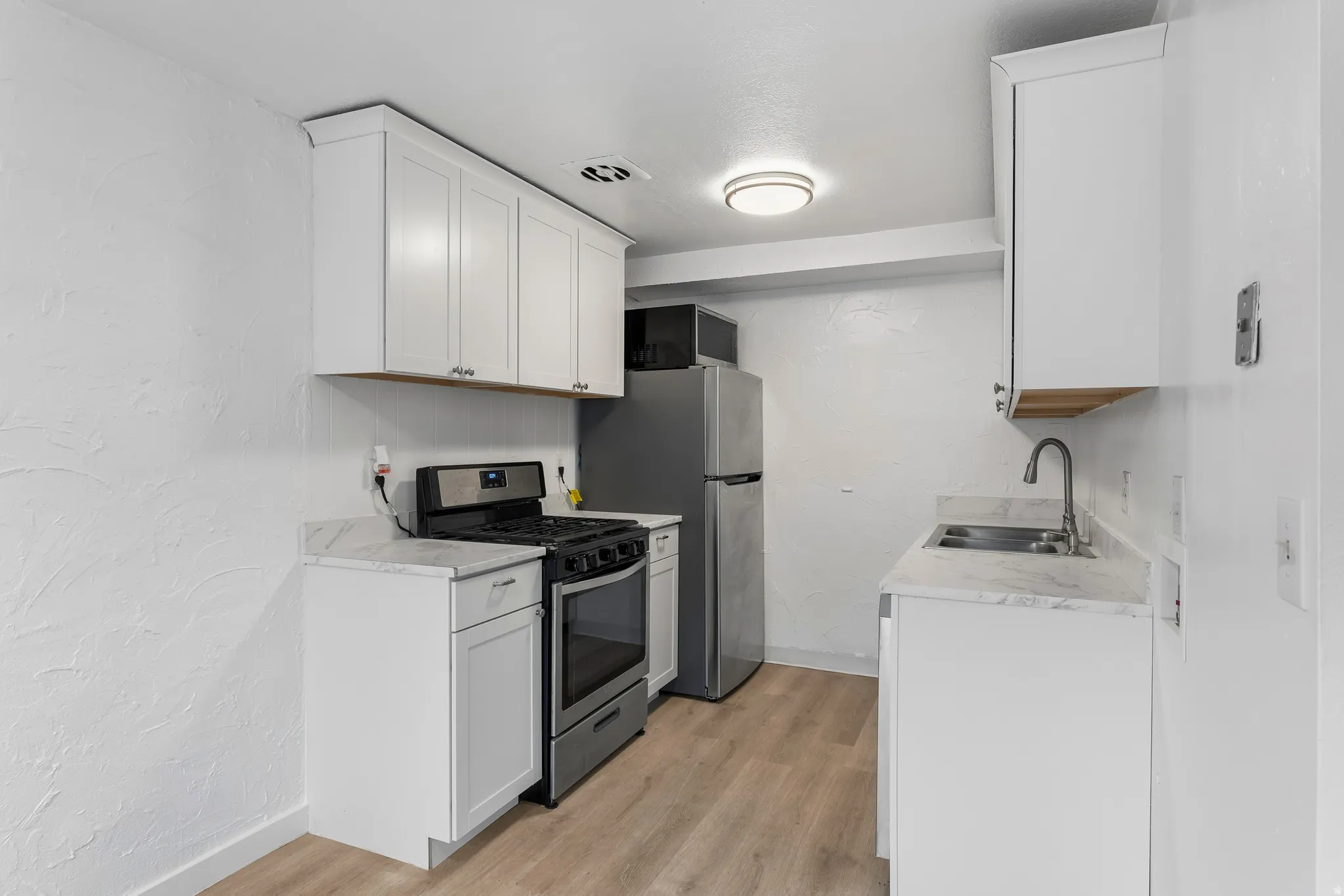 Kitchen featuring a textured wall, stainless steel gas range oven, white cabinetry, light countertops, and light wood-style flooring