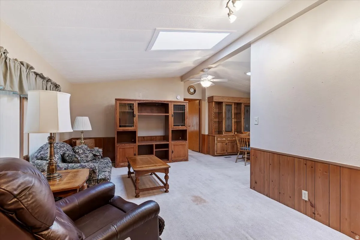 Carpeted living room featuring wooden walls, wainscoting, a skylight, and a ceiling fan