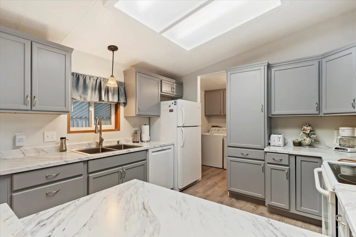 Kitchen with gray cabinetry, vaulted ceiling, white appliances, hanging light fixtures, and light wood-type flooring