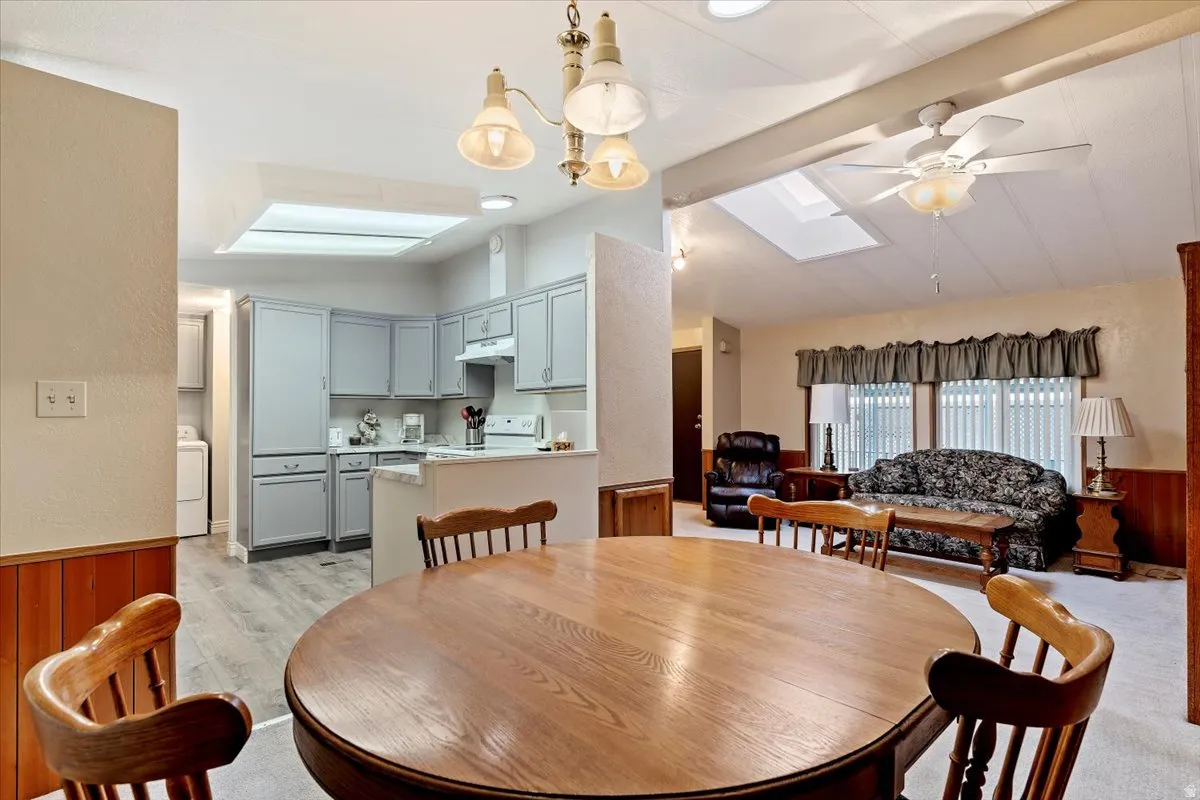 Dining room with a wainscoted wall, a skylight, wooden walls, vaulted ceiling, and a ceiling fan