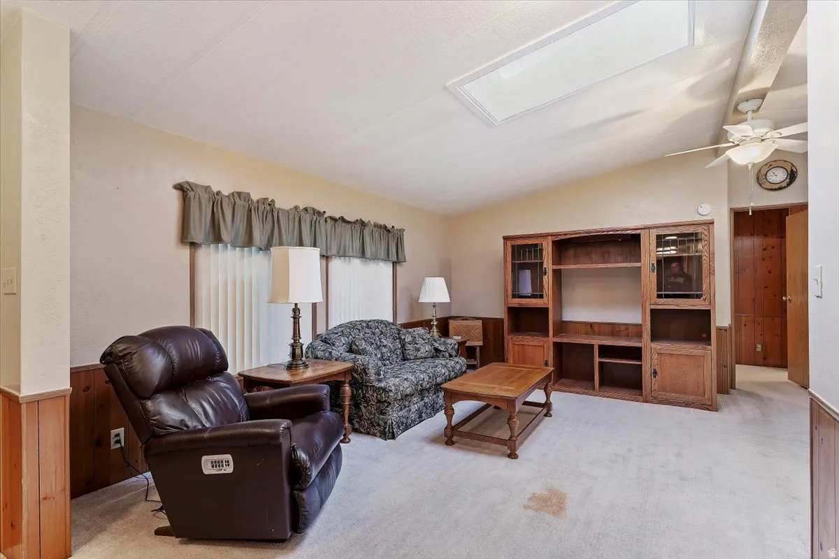 Living room featuring lofted ceiling, light colored carpet, a skylight, wooden walls, and a wainscoted wall