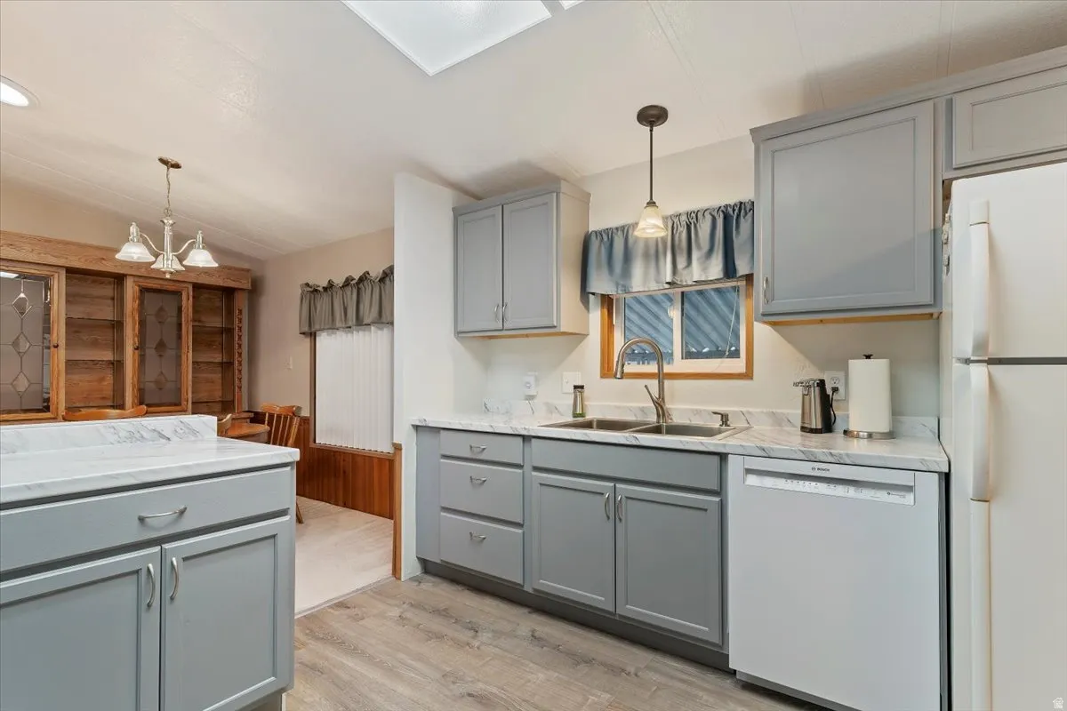 Kitchen with gray cabinetry, white appliances, decorative light fixtures, light wood finished floors, and a skylight