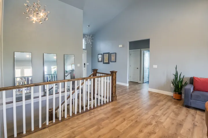 Corridor featuring a chandelier, an upstairs landing, high vaulted ceiling, and light wood-style flooring