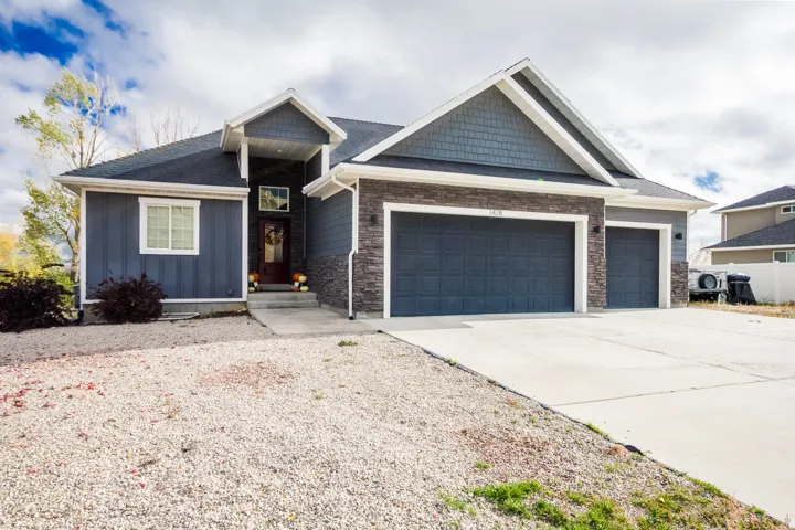 View of front of property featuring driveway, stone siding, an attached garage, and board and batten siding