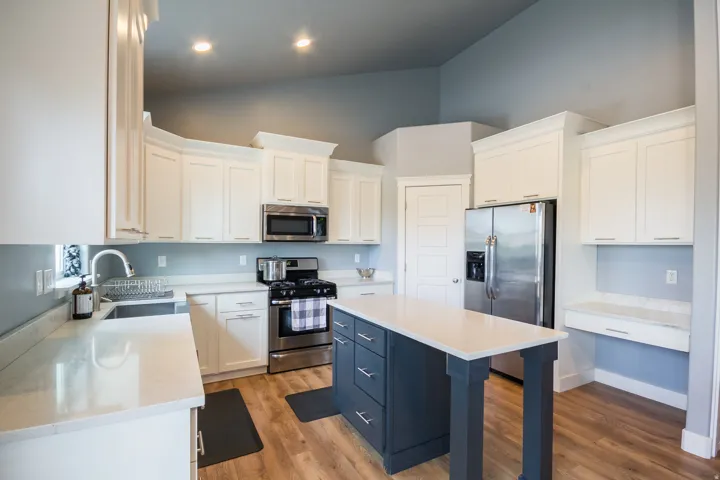 Kitchen with stainless steel appliances, high vaulted ceiling, white cabinetry, light stone counters, and light wood-style floors