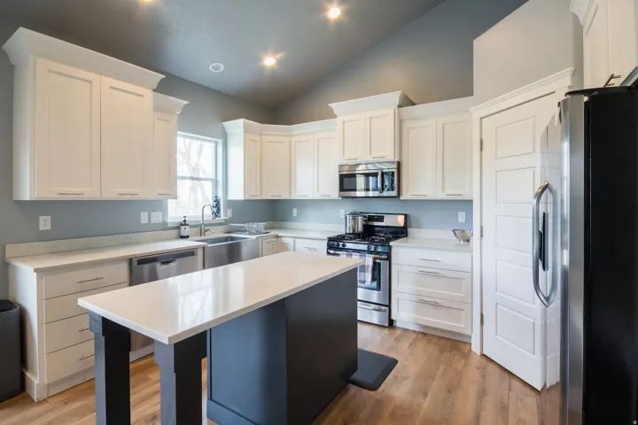Kitchen featuring stainless steel appliances, white cabinets, lofted ceiling, a kitchen island, and light wood-style floors