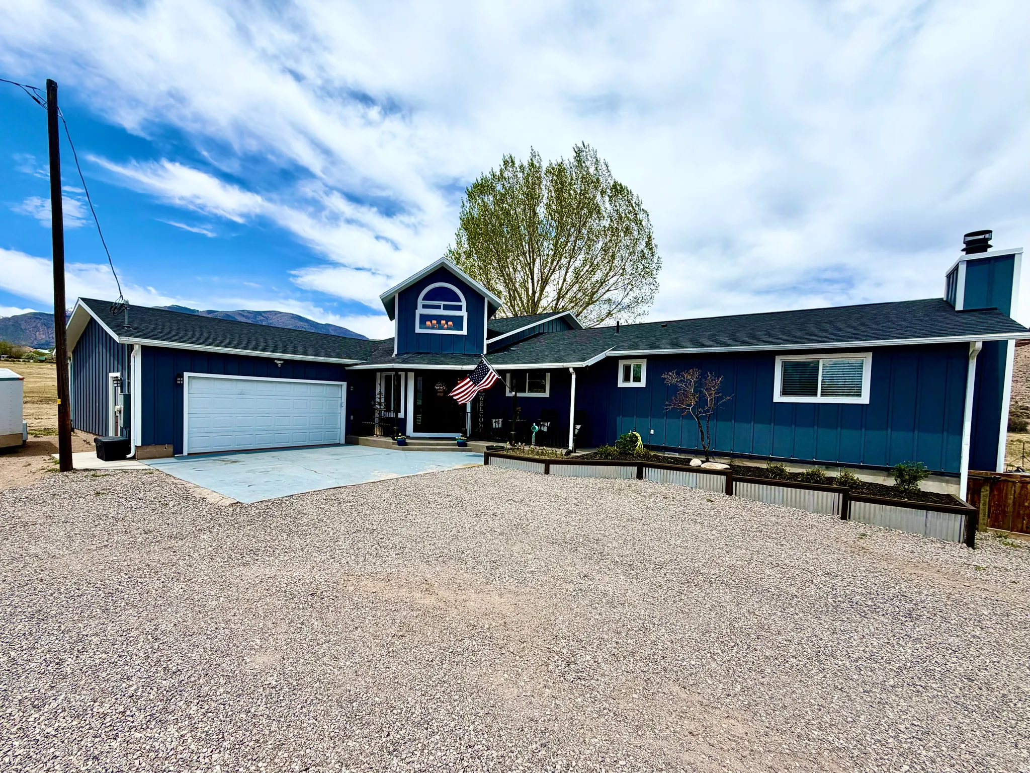 Navy blue exterior siding with white trim, a prominent two-car garage, and a gravel driveway