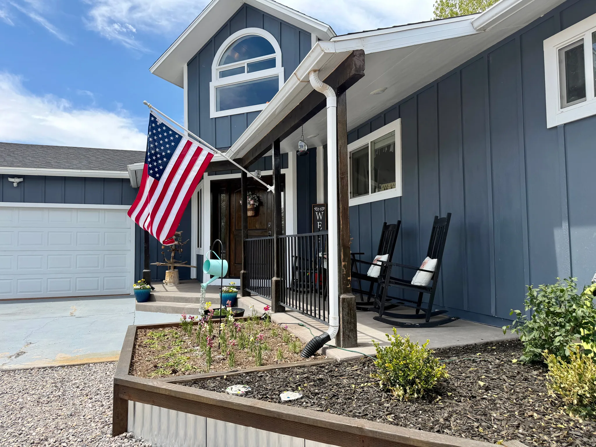 Exterior featuring a board-and-batten facade in a deep blue hue, a white paneled garage door, and a covered front porch