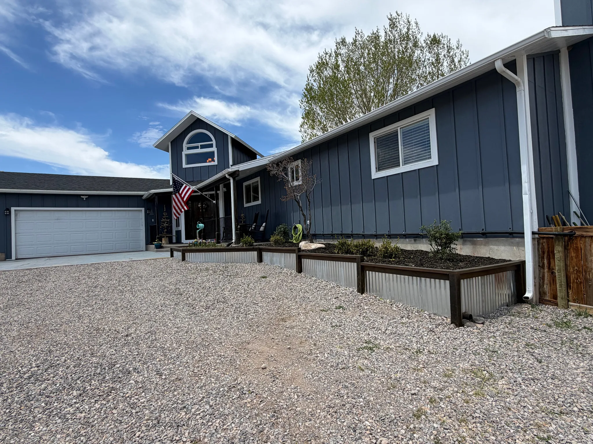Board-and-batten siding with white trim, a large two-car garage, and a gravel driveway