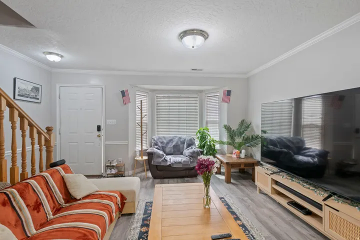 Living area with a textured ceiling, ornamental molding, stairs, and wood finished floors