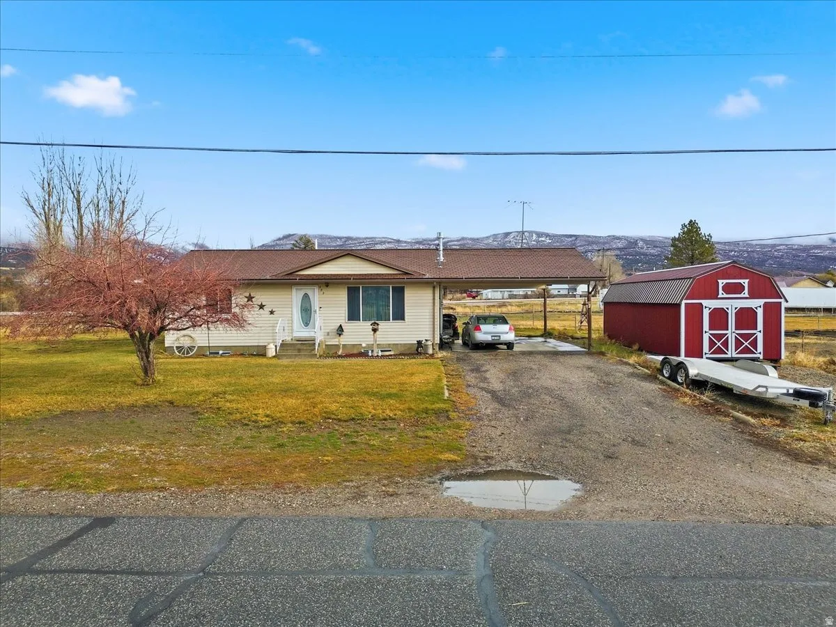View of front of home featuring driveway, a front yard, a storage unit, a carport, and entry steps