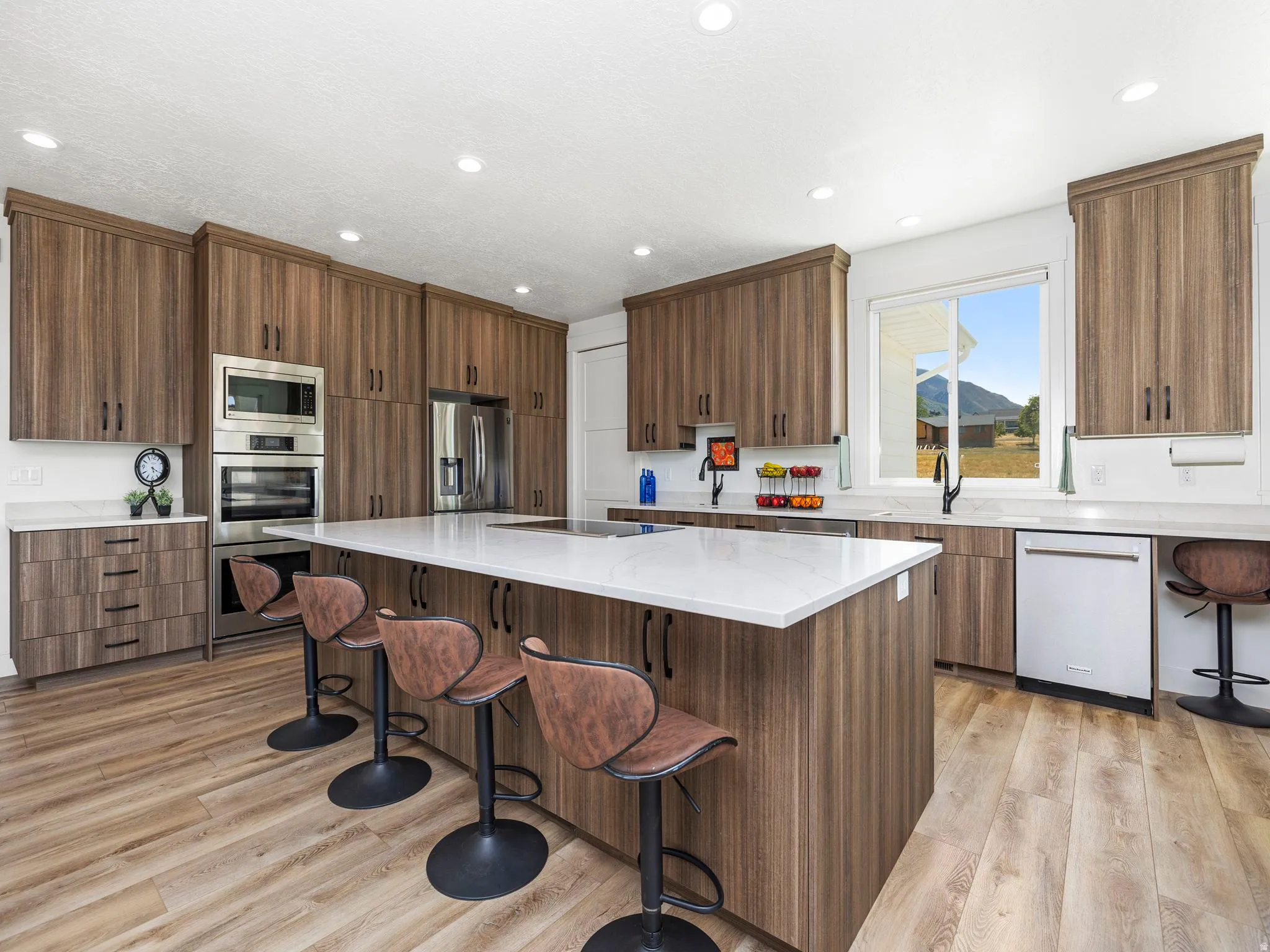 Kitchen featuring a breakfast bar area, light stone counters, stainless steel appliances, brown cabinetry, and modern cabinets