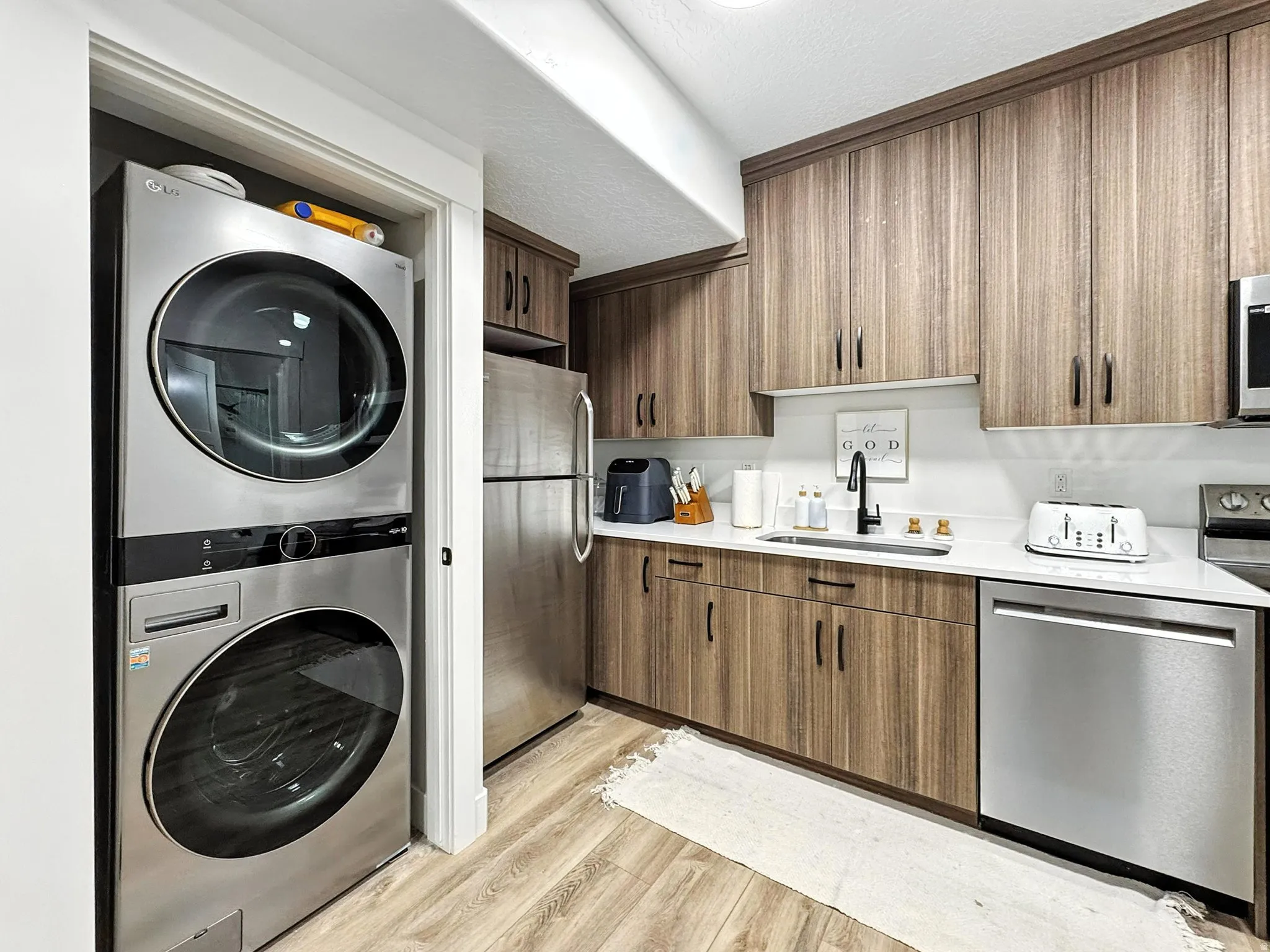 Basement apartment laundry area featuring stacked washer and clothes dryer and light wood finished floors
