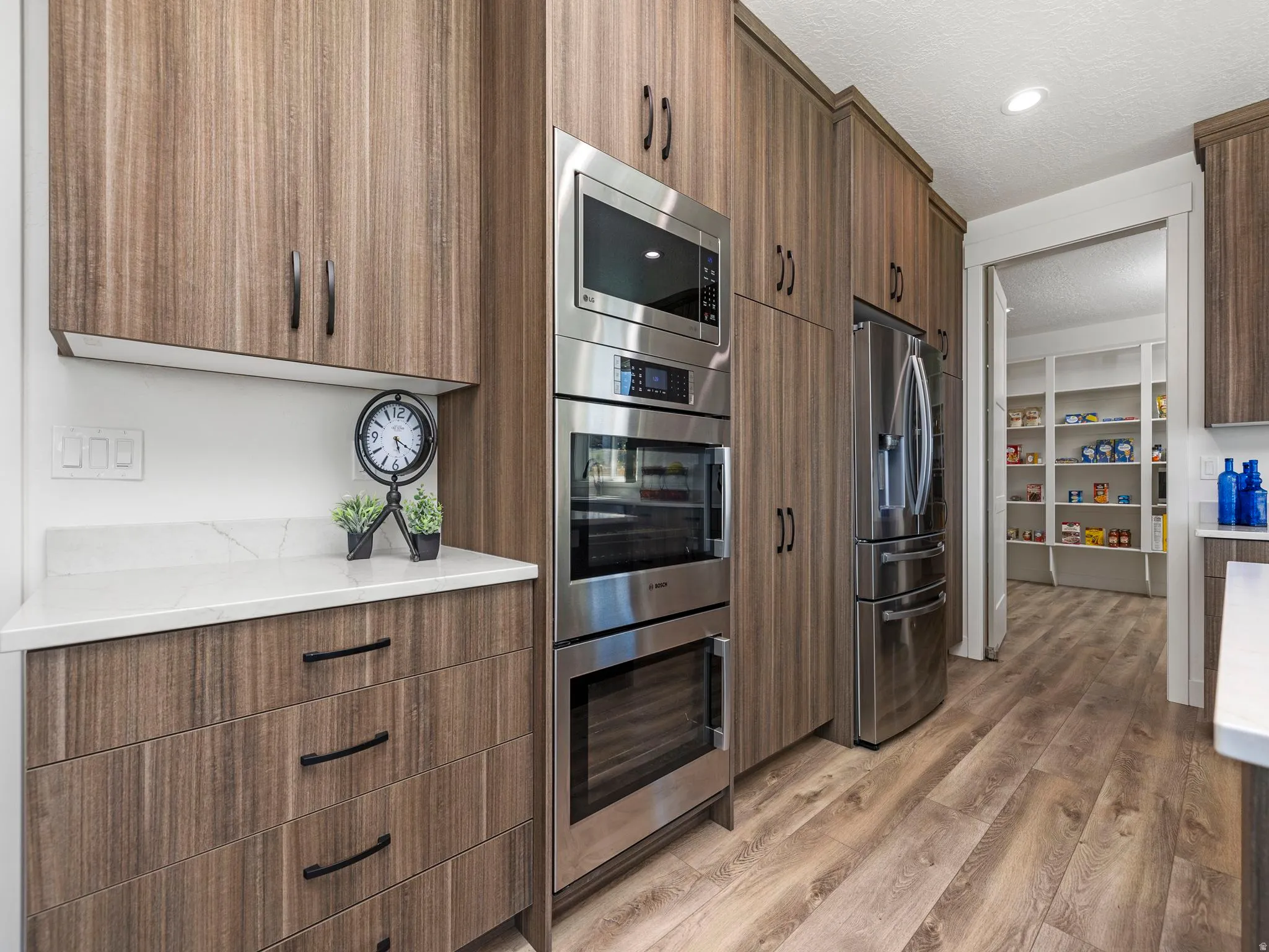 Kitchen with stainless steel appliances, double Bosch ovens, modern cabinets, light wood-style flooring, a textured ceiling, and light stone countertops