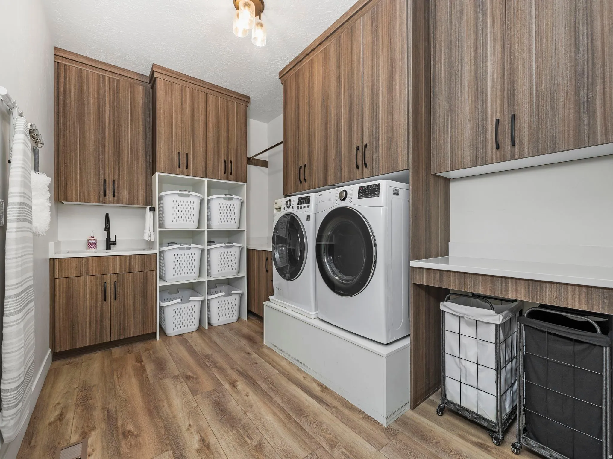 Washroom with a deep basin sink, cloths folding (and hanging) area, light wood-style flooring, a textured ceiling, cabinet space, and washer and clothes dryer (with built up pedestal and gas dryer)