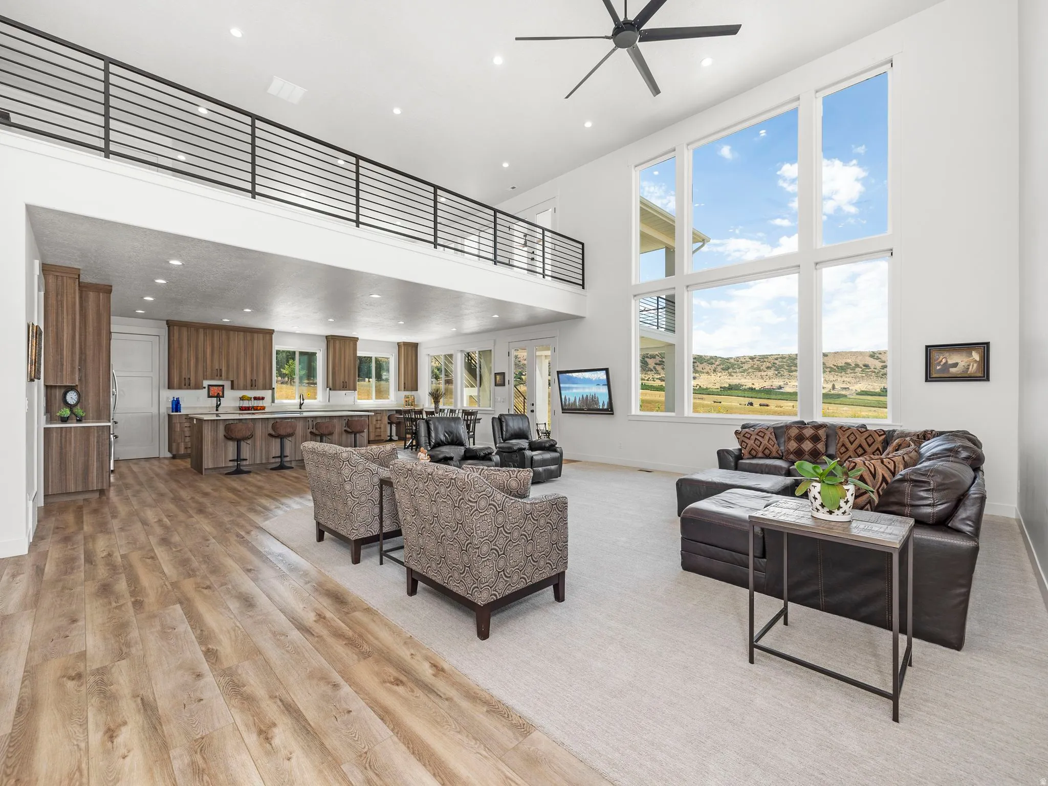 Living room with a high ceiling, light wood finished floors, recessed lighting, and a ceiling fan