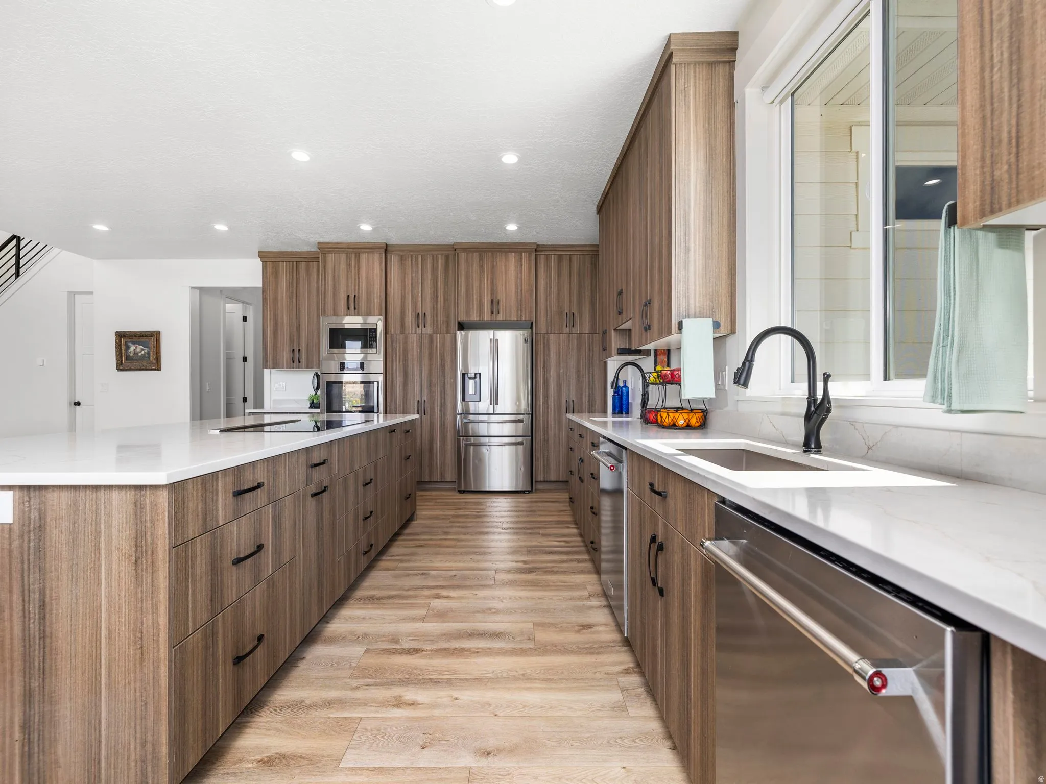 Kitchen with light stone countertops, appliances with stainless steel finishes, light wood-style flooring, recessed lighting, and brown cabinets