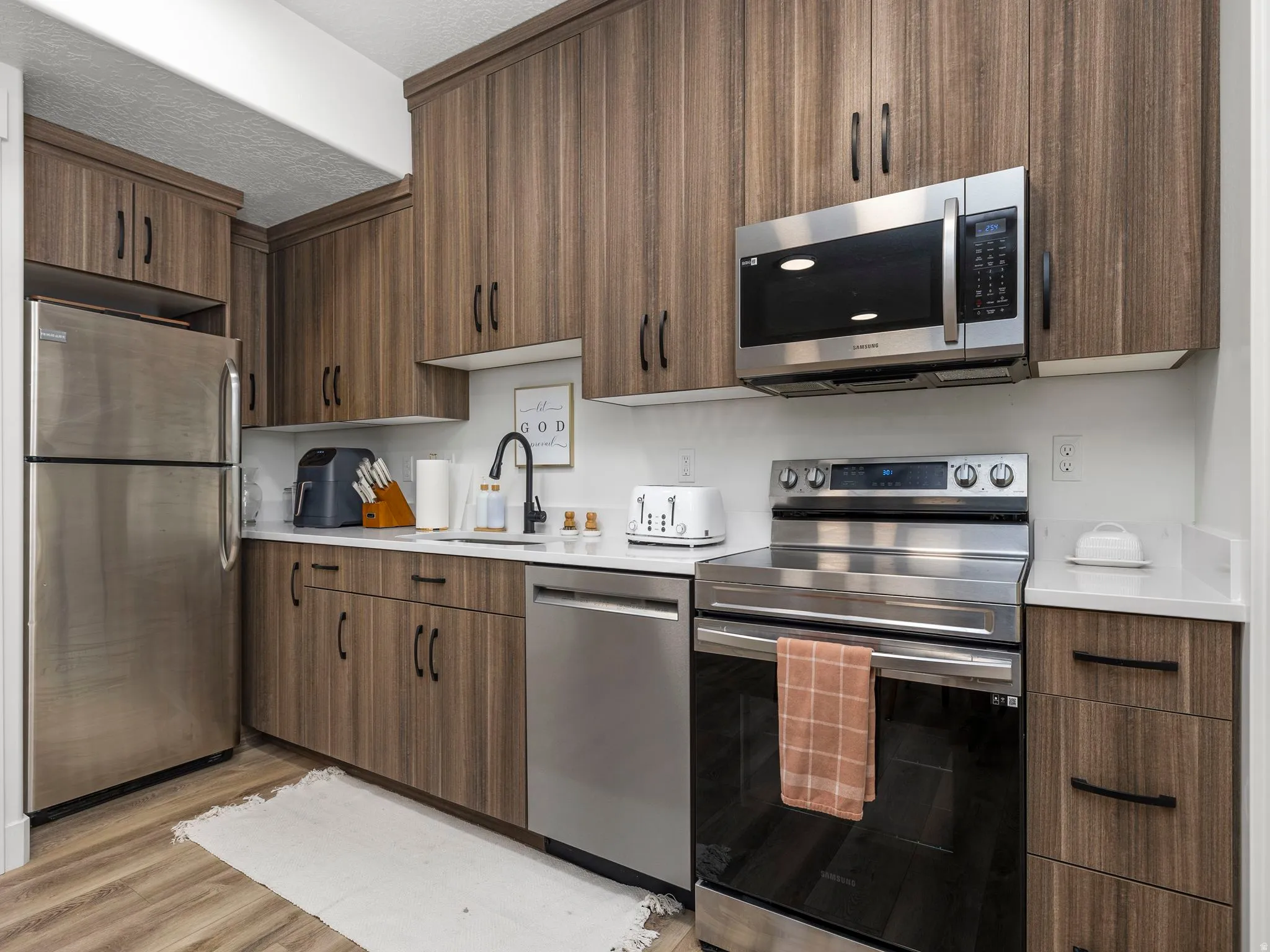 Basement apartment kitchen with stainless steel appliances, light wood-style flooring, light stone countertops, and modern cabinets