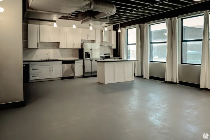 Kitchen featuring appliances with stainless steel finishes, dark countertops, white cabinets, wall chimney range hood, and concrete flooring
