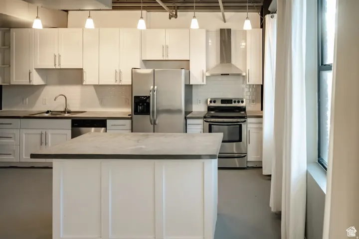 Kitchen with appliances with stainless steel finishes, wall chimney exhaust hood, white cabinets, and a kitchen island