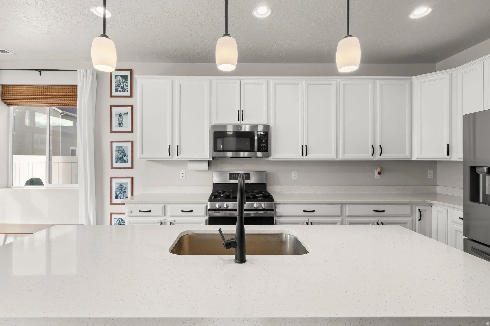 Kitchen with pendant lighting, stainless steel appliances, white cabinetry, light stone countertops, and recessed lighting