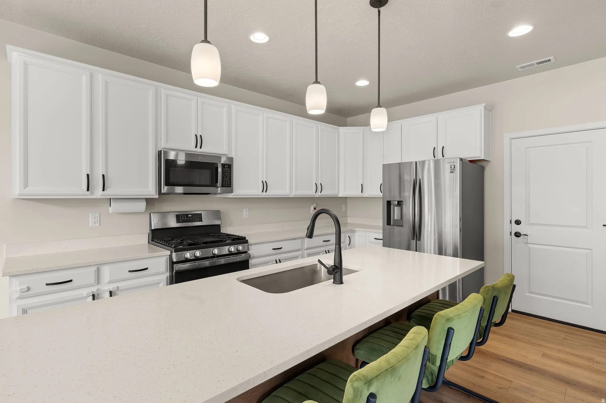 Kitchen featuring appliances with stainless steel finishes, white cabinets, a breakfast bar area, hanging light fixtures, and recessed lighting