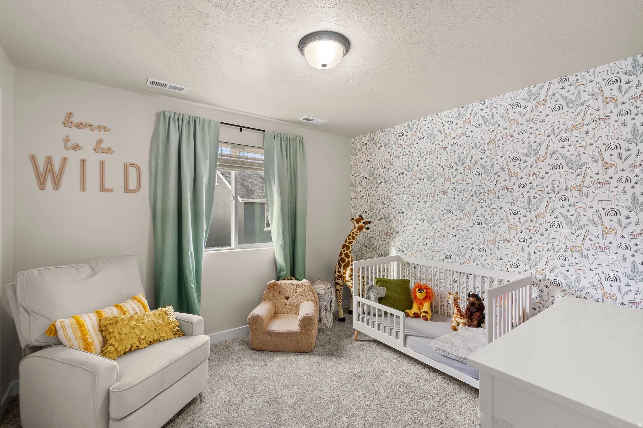 Carpeted bedroom with a textured ceiling, an accent wall, and a crib