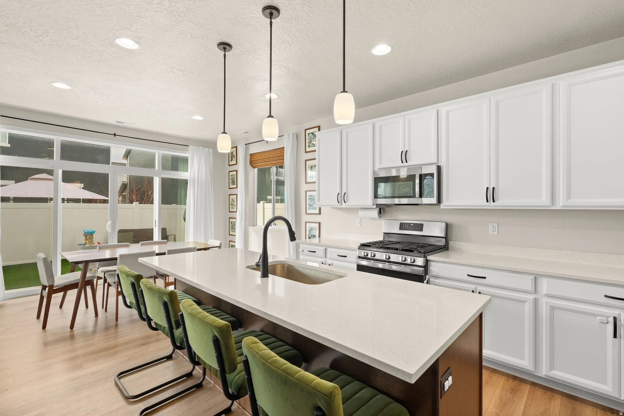Kitchen featuring white cabinetry, a textured ceiling, appliances with stainless steel finishes, light stone countertops, and light wood finished floors