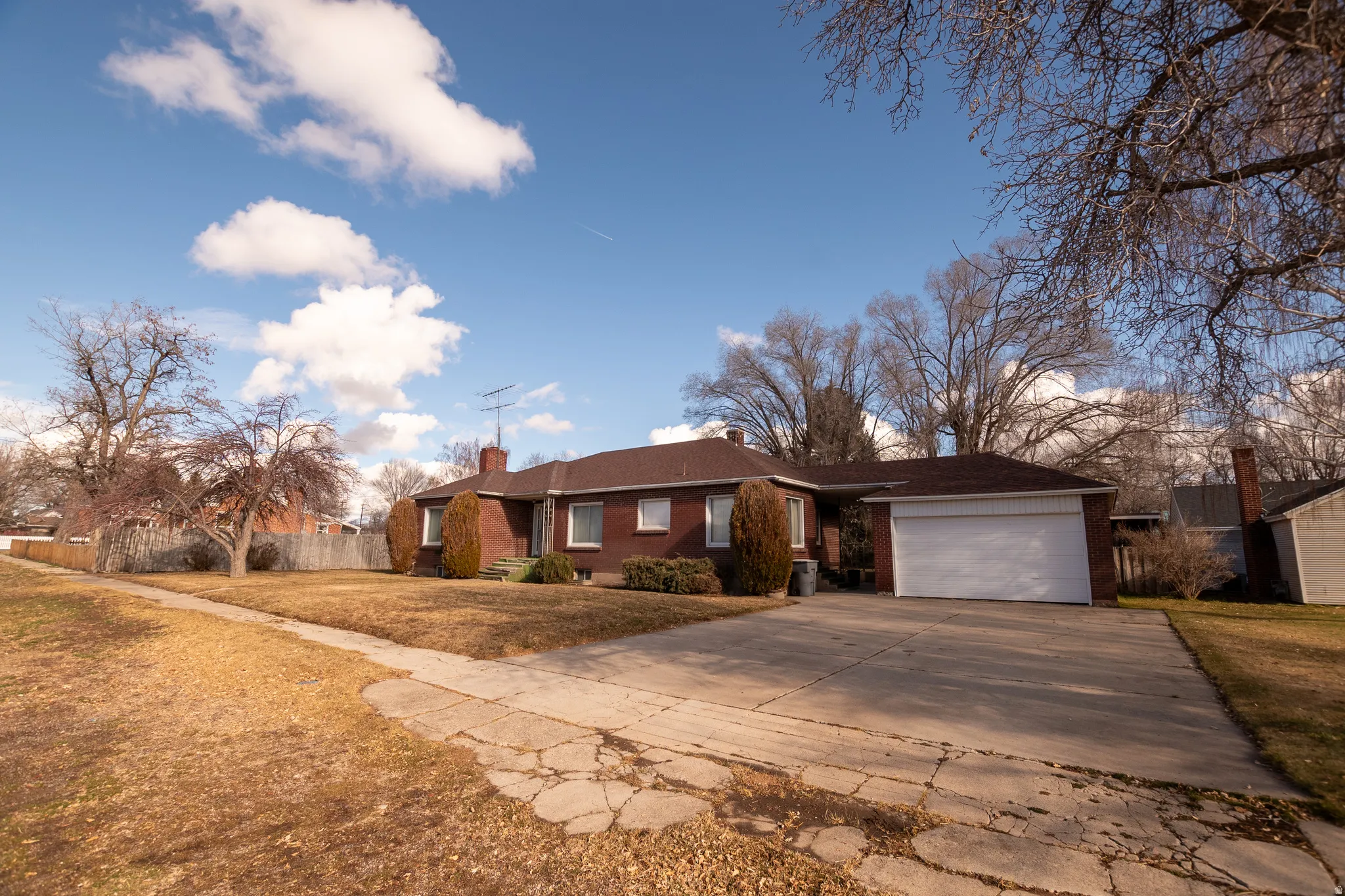 Single story home featuring brick siding, a front lawn, a chimney, concrete driveway, and an attached garage