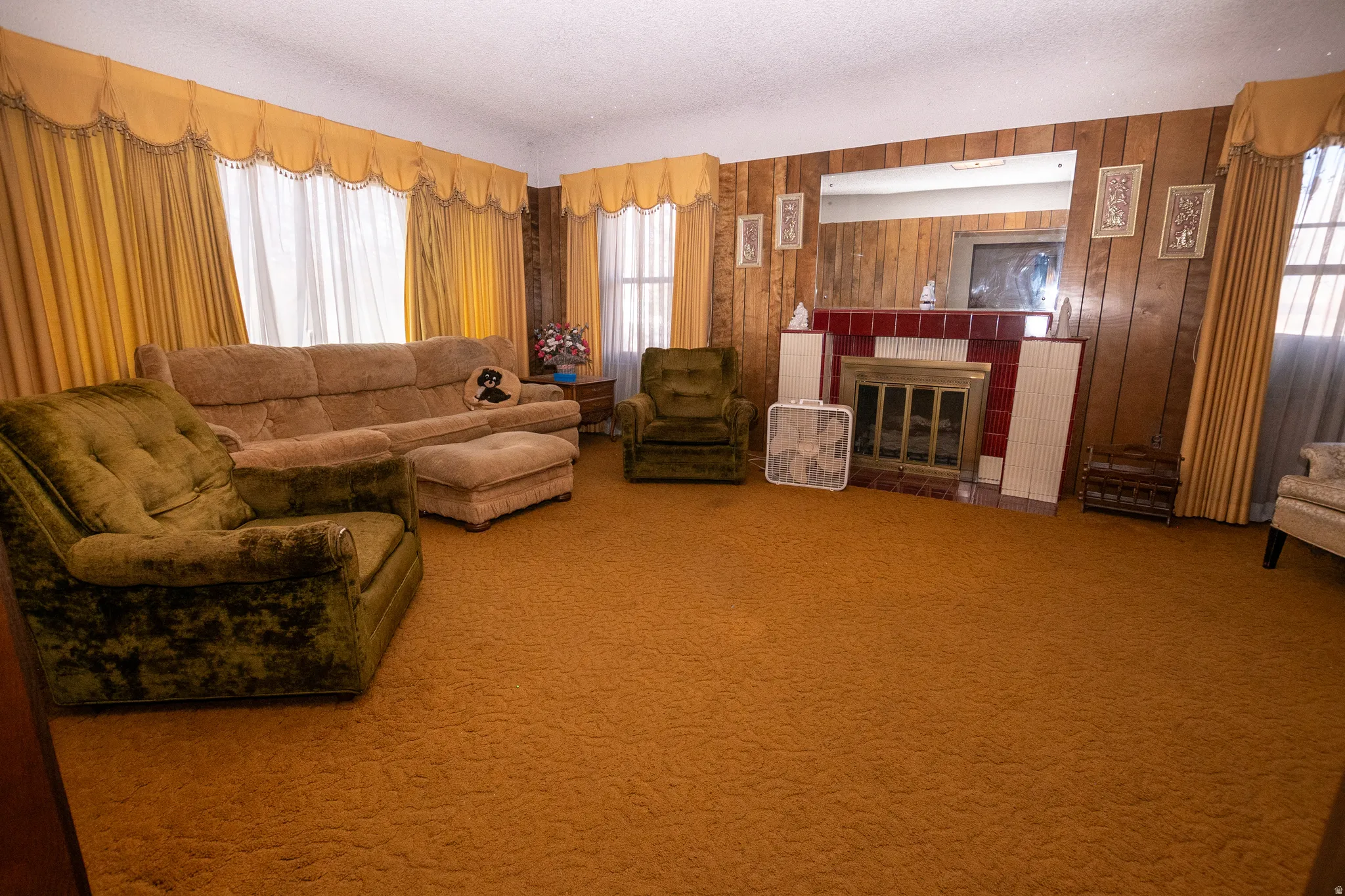 Carpeted living room with a tiled fireplace, a textured ceiling, and wood walls