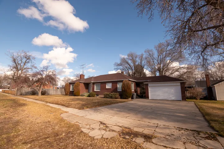 Single story home featuring brick siding, a front lawn, a chimney, concrete driveway, and an attached garage